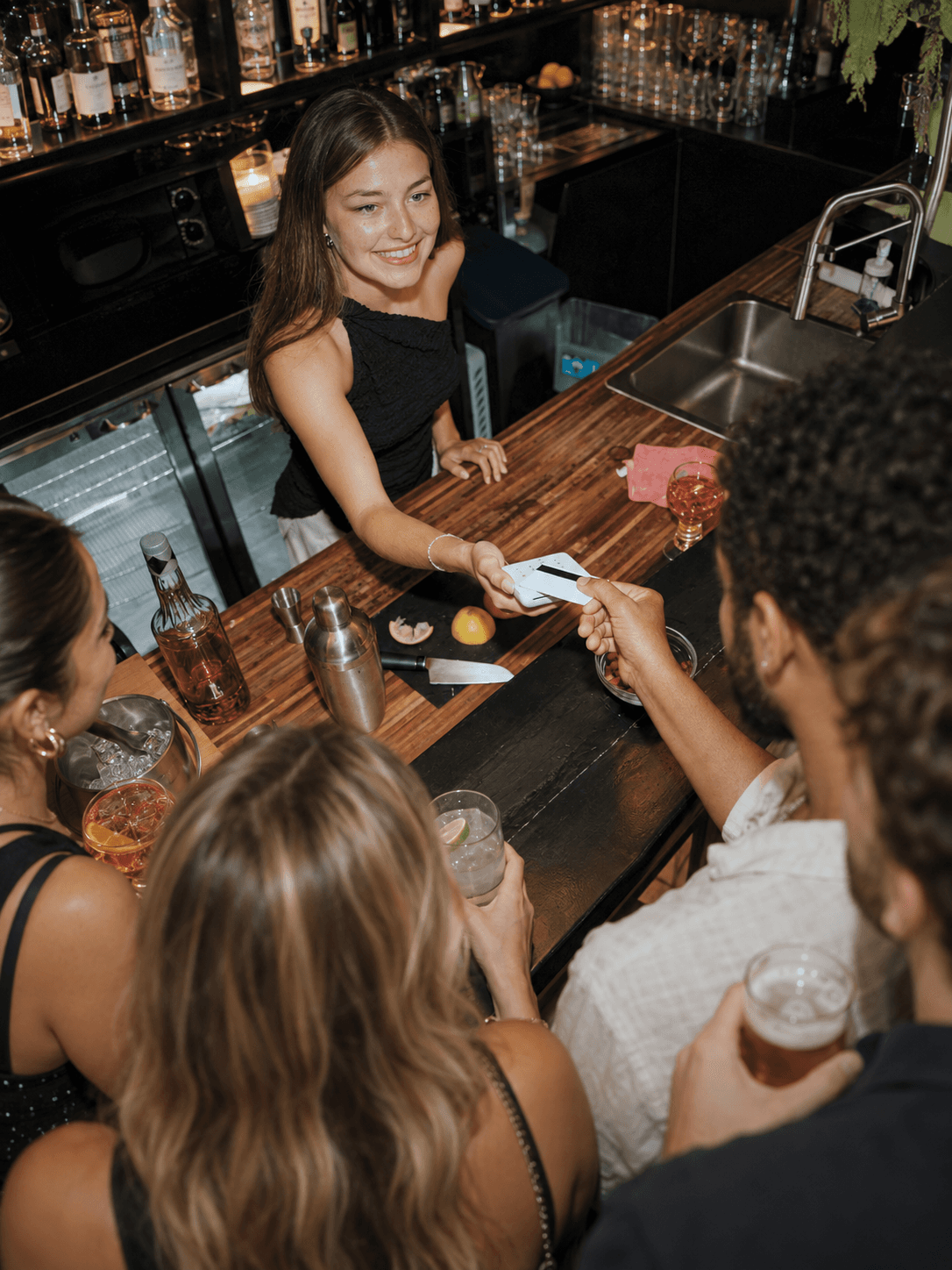 Ragazza sorridente al bancone che gestisce un pagamento su un POS bianco davanti a più clienti.